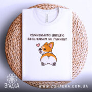 Футболка сумненькою дупцею не пукнеш. Біла футболка, складена на плетеному кошику, з принтом корги, що повертається, на фоні світлого кольору. Принт зображує корги з сердечком, що виглядає мило.