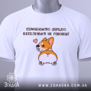 Футболка сумненькою дупцею не пукнеш. Біла футболка, складена на столі з легким блиском. Принт корги з сердечком на фоні світлого кольору, з етикеткою, що звисає з коміра.