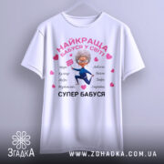 Футболка супер бабуся, біла, зображена на манекені, фон світло-сірий, принт з бабусею в синьому костюмі, що тримає табличку, оточена сердечками та словами, що описують її якості.