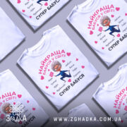 Футболка супер бабуся, біла, зображена на манекені, фон світло-сірий, принт з веселою бабусею в синьому костюмі, що тримає табличку з написом, оточена сердечками та словами, що описують її якості.