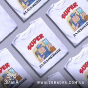Футболка супер далекобійник білого кольору, зображена з фронтального ракурсу на манекені, фон нейтральний, принт з мультяшним водієм у синій кепці та жовтій футболці, текст 'SUPER ДАЛЕКОБІЙНИК' червоного кольору.