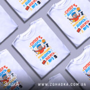 Футболка супер дідусь герой, біла, зображена з правого ракурсу, на фоні світло-сірого кольору, принт містить яскраві кольори з малюнком дідуся в червоному плащі, який тримає шахову фігуру та медаль.