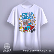 Футболка супер дідусь білого кольору, зображена з фронтального ракурсу на вішалці, фон світло-сірий, принт з дідусем у червоному плащі та хлопчиком, що піднімає руку, оточений зірками та трофеєм.