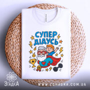 Футболка супер дідусь білого кольору, зображена зверху на плетеній кошику, фон світло-сірий, принт яскравий з дідусем та хлопчиком, деталі принта чіткі та кольорові.