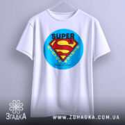 Футболка супер дідусь, біла, підвішена на вішалці, фон світло-сірий, принт у вигляді логотипу супермена, текст 'SUPER' та 'Наші дідусі' внизу.