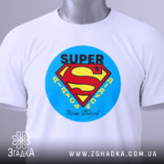 Футболка супер дідусь, біла, складена на столі, фон світло-сірий, принт з логотипом супермена, текст 'SUPER' та 'Наші дідусі' під ним, з етикеткою на рукаві.