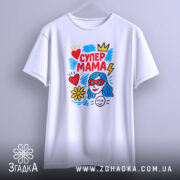 Футболка супер мама, білого кольору, підвішена на вішалці, фон світло-сірий, принт яскравий з червоним, жовтим, блакитним кольорами, зображує жінку з блакитним волоссям у червоних окулярах, серце, квітка та блискавка.