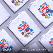 Футболка супер мама, білого кольору, зображена на манекені з правого боку, фон світло-сірий, принт містить яскраві кольори: червоний, жовтий, блакитний, з малюнком жінки з блакитним волоссям у червоних окулярах, серце, квітка та блискавка.