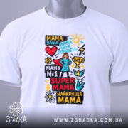 Футболка супер мама, біла, складена на столі, фон світло-сірий, принт кольоровий з текстом та малюнками, прикріплена етикетка зеленого кольору.
