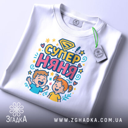 Футболка супер няня, білого кольору, складена на поверхні, фон світло-сірий, принт з дітьми та написом 'СУПЕР НЯНЯ', з етикеткою на рукаві.