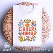 Футболка супер няня білого кольору, складена на плетеній основі, з принтом, що містить малюнки дітей та іграшок, розташованим по центру.