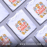 Футболка супер няня білого кольору, зображена на манекені, з принтом, що містить малюнки дітей, іграшок та сердець, розташованим по центру.