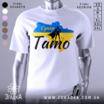 Футболка супер тато білого кольору, зображена на манекені, фон світло-сірий, принт включає синій та жовтий кольори з силуетом супергероя та написом 'Супер Тато'.