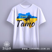 Футболка супер тато білого кольору, підвішена на вішалці, фон світло-сірий, принт з синім та жовтим кольорами, силует супергероя та напис 'Супер Тато'.