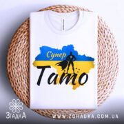 Футболка супер тато білого кольору, складена на плетеній основі, фон білий, принт з синім та жовтим кольорами, силует супергероя та напис 'Супер Тато'.