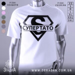 Футболка супер тато супермен, біла, зображена з близького ракурсу, на манекені, фон світло-сірий, принт чорний з великим літерою 'S' та написом 'СУПЕРТАТО'.