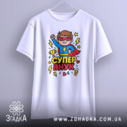 Футболка супер внук білого кольору, підвішена на вішалці, фон світло-сірий, принт з супергероєм у червоному плащі, що піднімає кулак, оточений блискавками та сердечками.