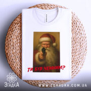 Футболка суворий Санта, біла, складена на плетеній основі, фон світлий, принт з зображенням Санти з пістолетом, текст червоним шрифтом "ТИ БУВ ЧЕМИМ?".