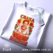 Футболка сваха подарунок, біла, зображена з верхнього ракурсу, фон світлий, принт з жінкою в українському вбранні, червоні троянди, на футболці є етикетка з логотипом.