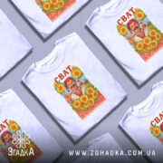 Футболка сват білого кольору, зображена на манекені, фон світло-сірий, принт з усміхненим чоловіком у традиційному вбранні на фоні соняшників та церкви, напис 'СВАТ' червоним кольором вгорі.