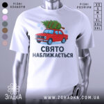 Футболка свято наближається. Біла футболка з коротким рукавом, зображення червоного автомобіля з ялинкою на даху, текст "СВЯТО НАБЛИЖАЄТЬСЯ" під малюнком, фон нейтральний, деталі принта яскраві.