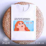 Футболка світла вже не треба. Біла футболка, складена на плетеній кошику, з видимим принтом. Фон світлий, з текстурою плетеного кошика. Принт з ілюстрацією дівчини з рудим волоссям, текст на українській мові розташований над малюнком.
