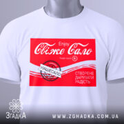 Футболка свіже сало білого кольору, складена на поверхні, з принтом червоного кольору, на якому написано "Свіже сало" та інші деталі, на футболці є зелений ярлик, фон світлий.