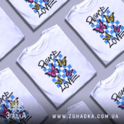 Футболка свобода любові. Білий колір, зображена на манекені з правого боку, фон світло-сірий. Принт містить три метелики: два рожевих та один жовтий, на фоні з блакитних квадратів, текст 'PEACE LOVE' написаний чорним шрифтом.