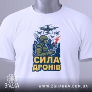 Футболка сила дронів, біла, зображена зверху, фон світло-сірий, принт з військовим, що керує дронами, з написом 'СИЛА ДРОНІВ' у жовтому кольорі, з етикеткою на шнурку.