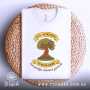 Футболка сила можливостей. Біла футболка, складена на плоскій поверхні з плетеного кошика. Принт з деревом та написом розташований по центру, фон світлий, а футболка має округлий виріз.