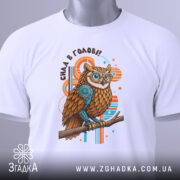 Футболка сила в голові, біла, зображена зверху, на ній прикріплений етикет, фон світлий, принт з совою з коричневим пір'ям та блакитними елементами, текст 'Сила в голові!!' над совою.