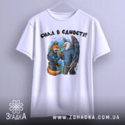 Футболка сила в єдності, біла, підвішена на вішалці, фон світло-сірий, принт з двома персонажами: лисицею та орлом, які стискають руки, на лисиці броня, на орлі светр.