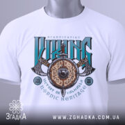 Футболка сила вікінга, біла, складена на столі, фон світло-сірий, принт з написом 'VIKING' у зелених та чорних кольорах, з зображенням щита та сокири, з етикеткою на зеленій стрічці.