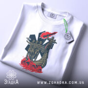 Футболка символ мужності. Білий колір, зображена на столі, ракурс зверху, фон світло-сірий, принт зображає фігуру жінки та чотирьох чоловіків на човні, з етикеткою, що звисає.