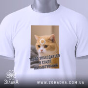 Футболка табло налаштовується, біла, зображена з верхнього ракурсу, фон світлий, принт з котом, на якому квітка на лобі та текст "ТАБЛЮ ЗНАХОДИТЬСЯ В СТАДІ НАЛАШТУВАННЯ", на комірці є етикетка.