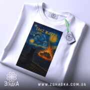 Футболка таке життя, біла, з верхнього ракурсу, на фоні світло-сірого кольору, складена, принт з зображенням кота на даху, текст 'ТАКЕ ЖИТТЯ' вгорі, з етикеткою на зеленому шнурку.