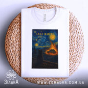 Футболка таке життя, біла, з верхнього ракурсу, на фоні плетеного кошика, складена, принт з зображенням кота на даху, текст 'ТАКЕ ЖИТТЯ' вгорі.