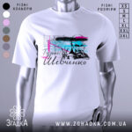 Футболка Тарас Григорович Шевченко, біла, зображена на манекені з блискучою поверхнею, фон світло-сірий, принт містить портрет Шевченка з кольоровими акцентами в блакитному та рожевому, текст на українській мові.