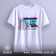 Футболка Тарас Григорович Шевченко, біла, підвішена на вішалці, фон світло-сірий, принт з портретом Шевченка, кольорові акценти в блакитному та рожевому, текст на українській мові.