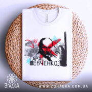 Футболка Тарас Шевченко білого кольору, зображена на плетеній основі, ракурс зверху, фон нейтральний, принт містить портрет Тараса Шевченка з червоними і блакитними акцентами, текстовий елемент.