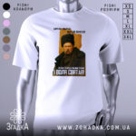 Футболка Тарас Шевченко борітеся, біла футболка з принтом, зображення Тараса Шевченка в чорній шапці, фон світло-сірий, текст на футболці чорний і жовтий, розташування принта по центру.