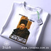 Футболка Тарас Шевченко борітеся, біла футболка, зображення Тараса Шевченка з принтом, футболка складена, фон білий, текст на футболці чорний і жовтий, етикетка зеленого кольору.