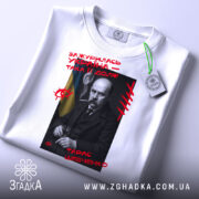 Футболка Тарас Шевченко подарунок, біла футболка з принтом, зображення Тараса Шевченка на чорному фоні, червоний текст з написом 'Зажурилась Україна – така її доля!', ракурс зверху, на футболці зелений ярлик.