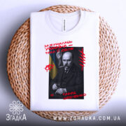 Футболка Тарас Шевченко подарунок, біла футболка з принтом, зображення Тараса Шевченка на чорному фоні, червоний текст з написом 'Зажурилась Україна – така її доля!', ракурс зверху, футболка лежить на плетеній основі.