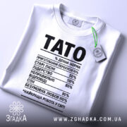 Футболка тато денна норма, біла, складена на поверхні, фон світлий, на комірці зелена етикетка, принт чорний з текстом, що містить різні відсотки і назви.