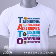 Футболка тато герой для дітей, біла, зображена зверху, на столі, фон світло-сірий, принт кольоровий з текстом "ТАТО" та іконками, на футболці є етикетка з логотипом.