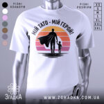 Футболка тато герой, біла, зображена на манекені, фон світло-сірий, принт з фігурами батька та дитини на фоні градієнту від оранжевого до рожевого.