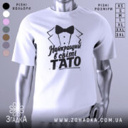 Футболка тато найкращий, біла, зображена з правого боку, фон світло-сірий, принт чорного кольору з текстом 'Найкращий в світі TATO' та малюнком смокінга.
