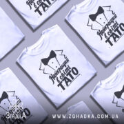 Футболка тато найкращий, біла, зображена з правого боку, фон світло-сірий, принт чорного кольору з текстом 'Найкращий в світі TATO' та малюнком смокінга.