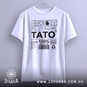 Футболка тато органічний, білого кольору, підвішена на вішалці, фон світло-сірий, принт чорного кольору з текстом і символами, футболка має вільний крій.